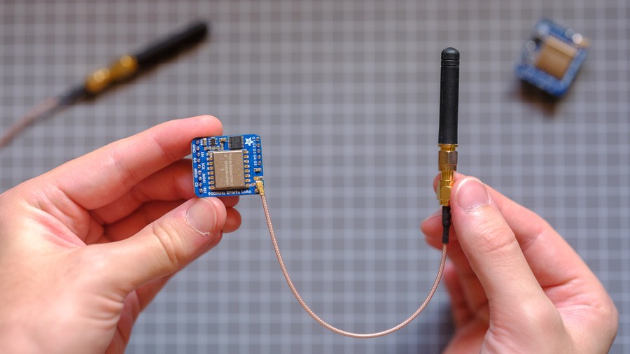 Hands holding blue PCB with metal shielding, antenna on short cable